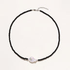 Beaded black agate necklace with iridescent baroque freshwater pearl centerpiece on cream background.