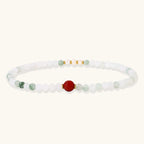 Three layered white beaded bracelets with carved orange agate lotus centerpiece and freshwater pearls on cream background.