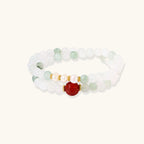 Three layered white beaded bracelets with carved orange agate lotus centerpiece and freshwater pearls on cream background.